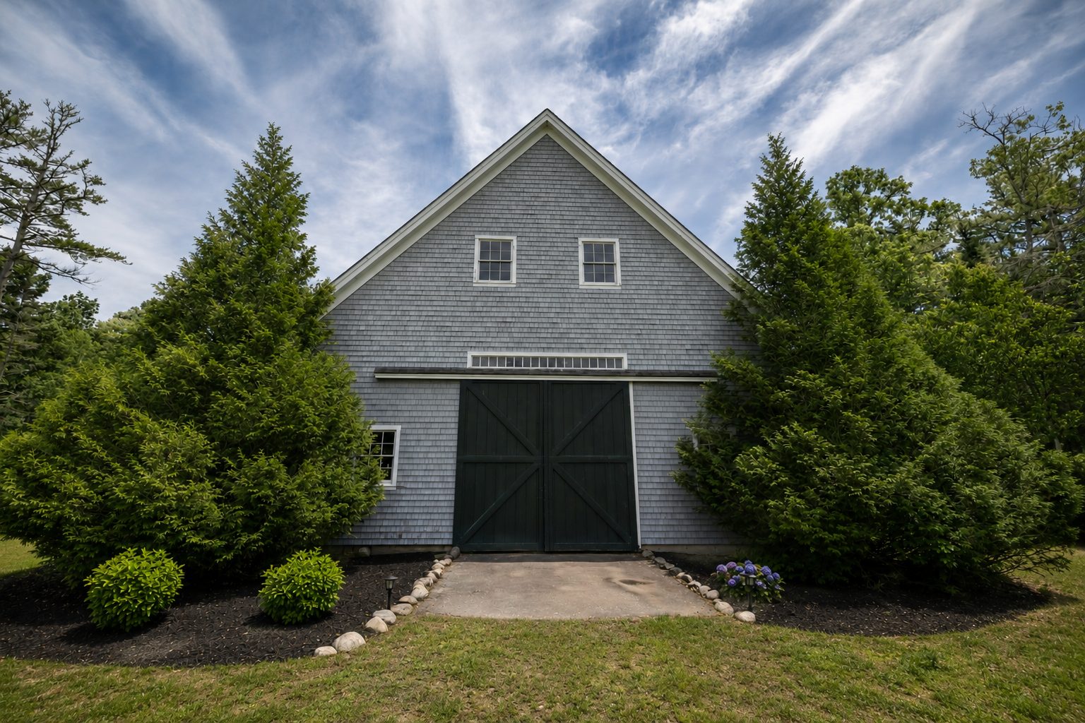 The barn's front doors framed by tall evergreens and hydrangeas