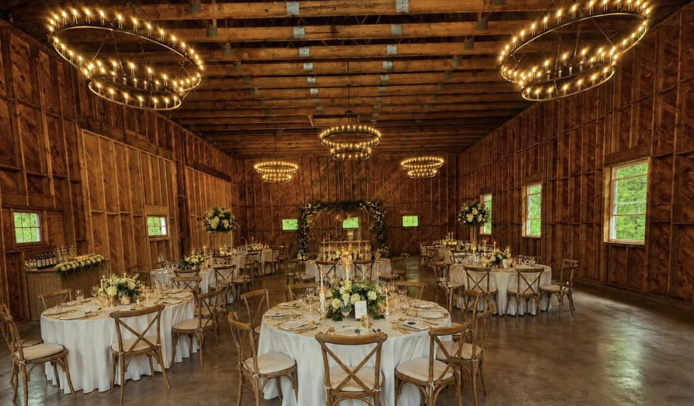 Reception inside the barn, wagon-wheel candle chandeliers lit above long tables set for dinner