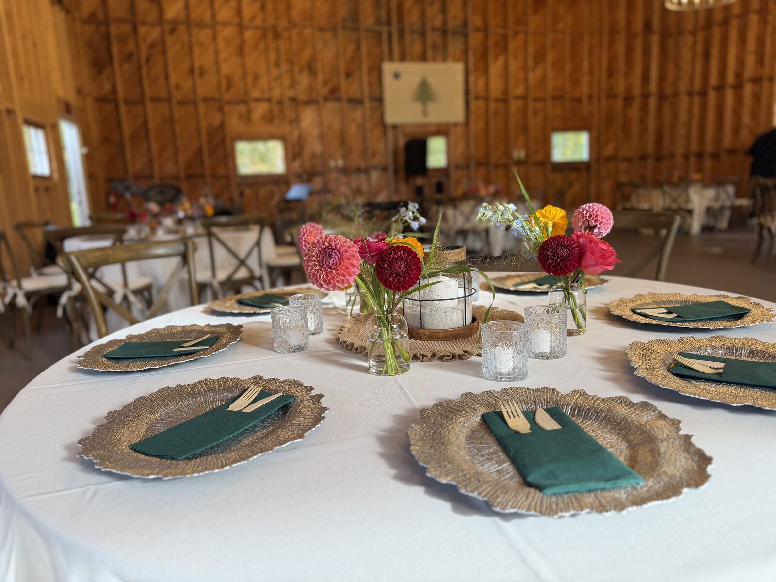 A round dinner table in the barn set with gold chargers, green napkins, and dahlia centerpieces