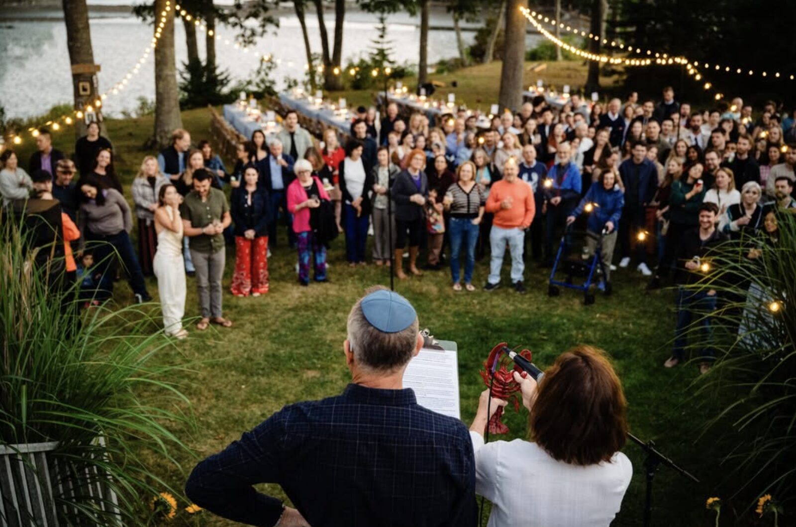 Guests gather on the string-lit waterfront lawn for a welcome toast before the lobster bake