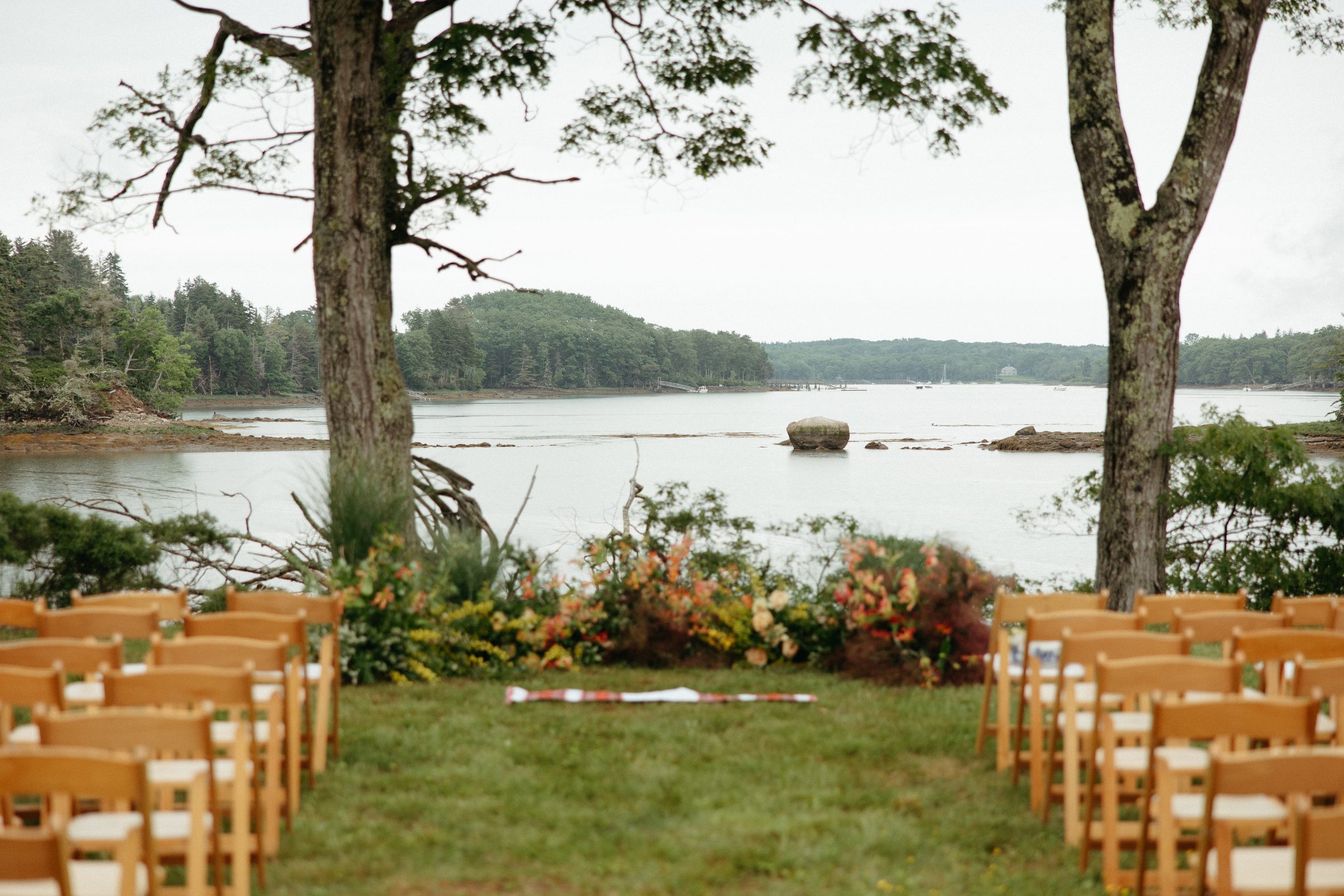Empty ceremony chairs facing the water, with a floral arrangement, before guests arrive
