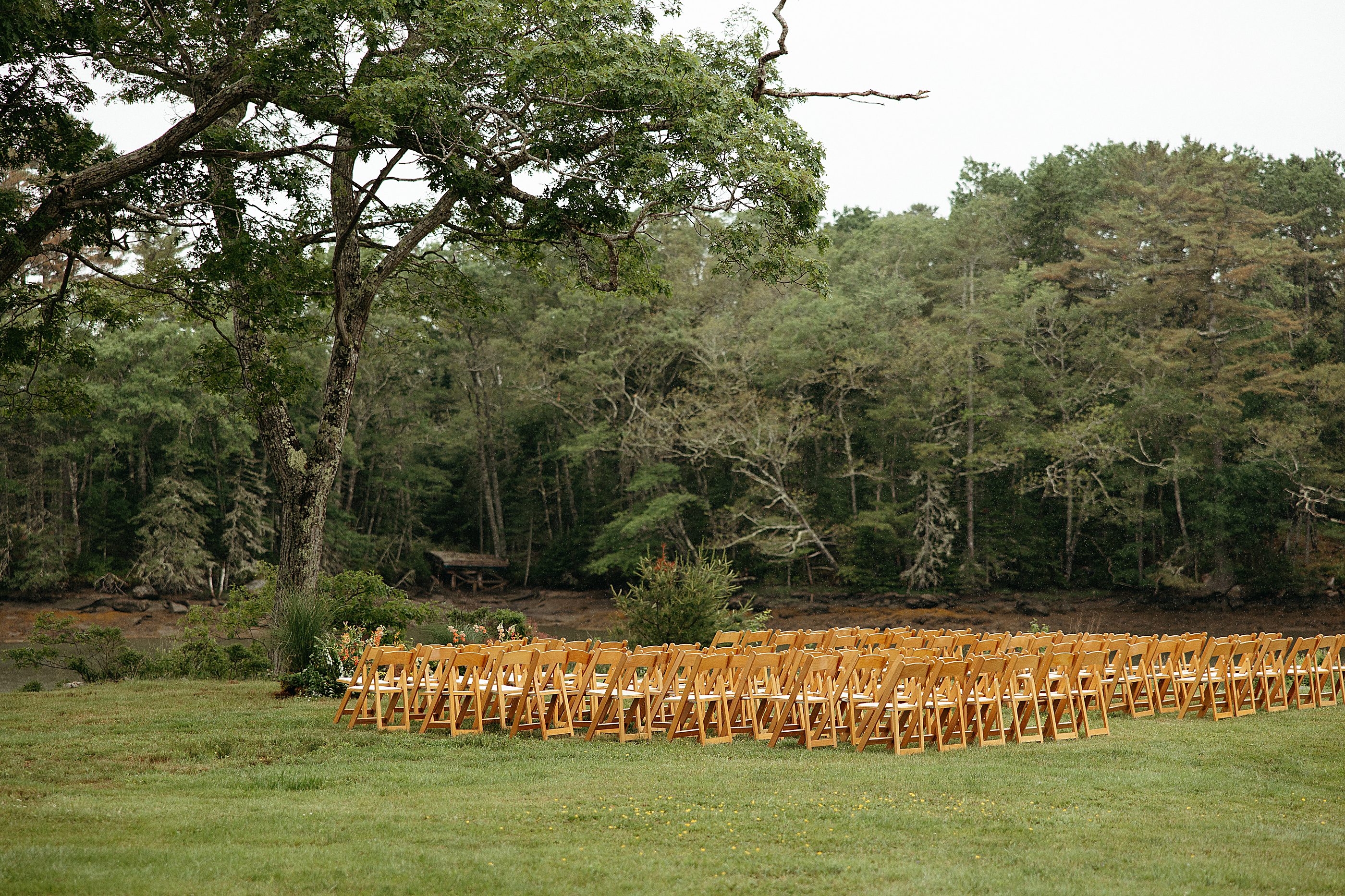 Rows of wooden ceremony chairs facing the harbor beneath a canopy of oak trees
