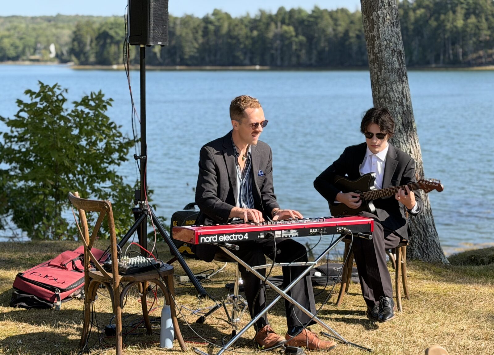 A keyboardist and guitarist play live music on the lawn with the harbor behind them