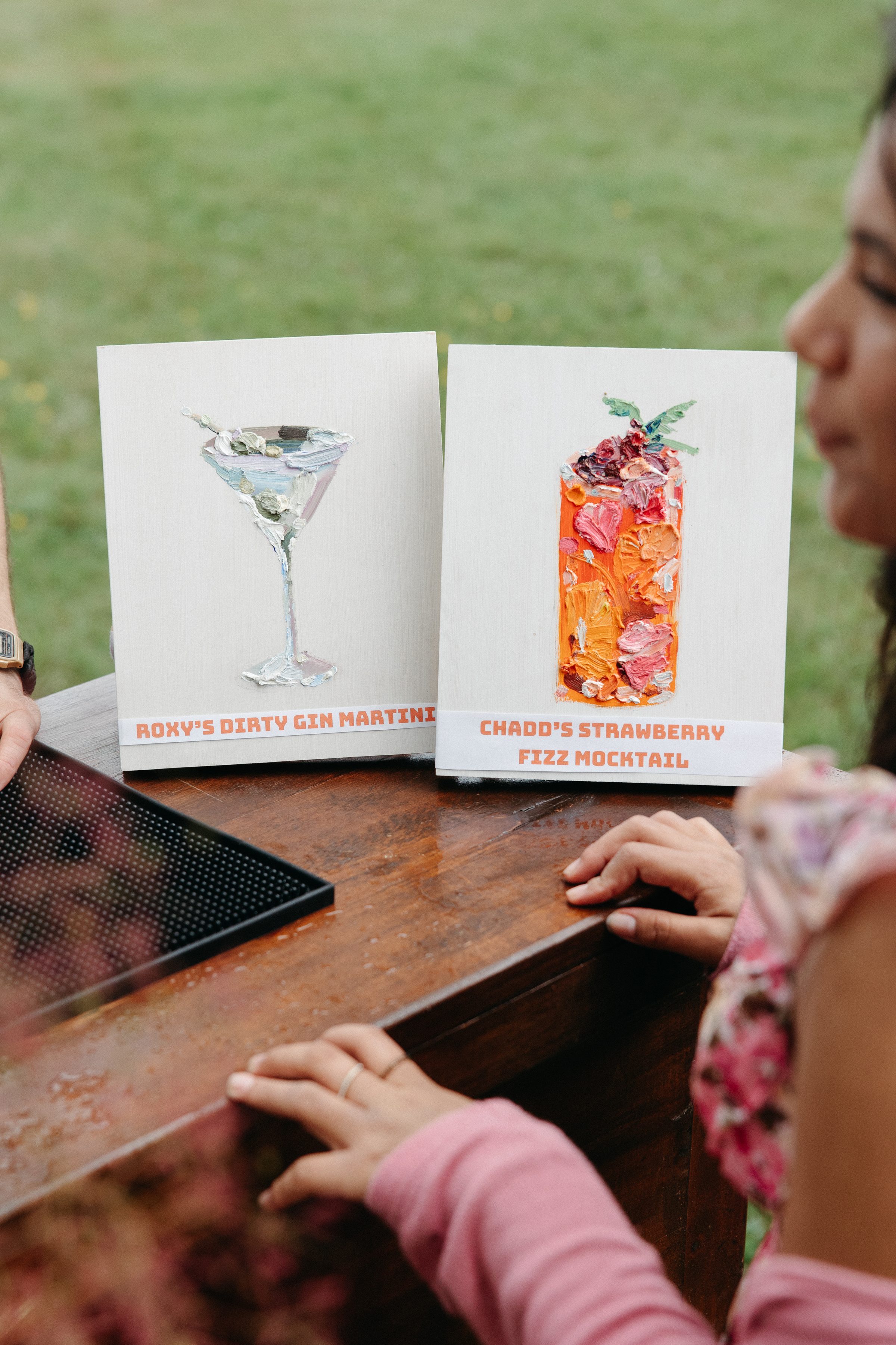 Hand-painted signature cocktail cards reading Roxy's Dirty Gin Martini and Chadd's Strawberry Fizz Mocktail