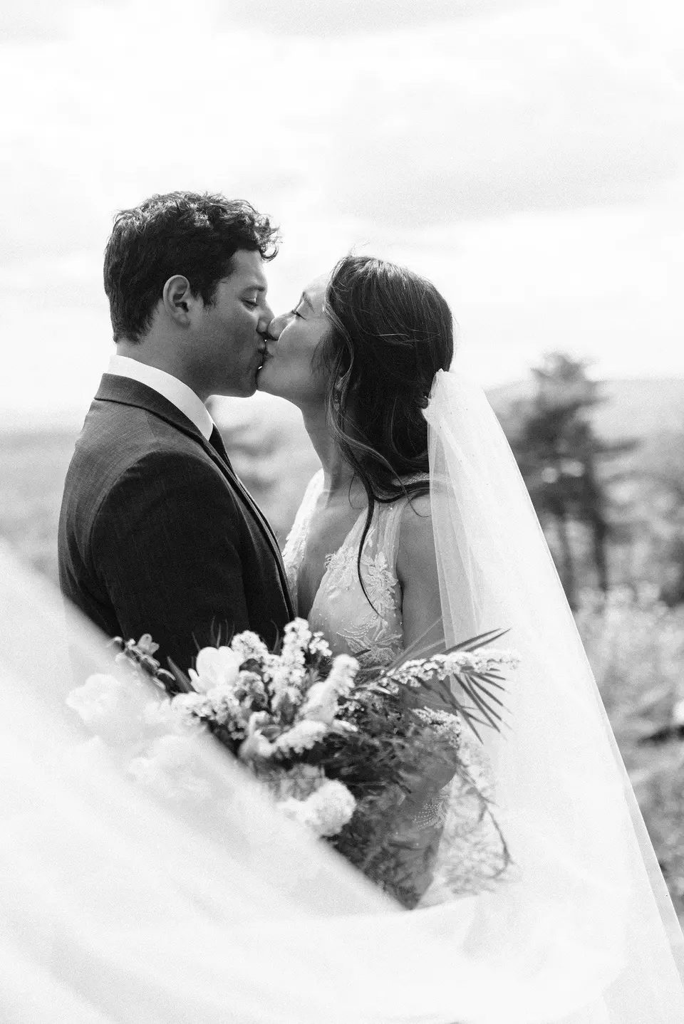 A bride and groom kiss under a veil, black and white photograph