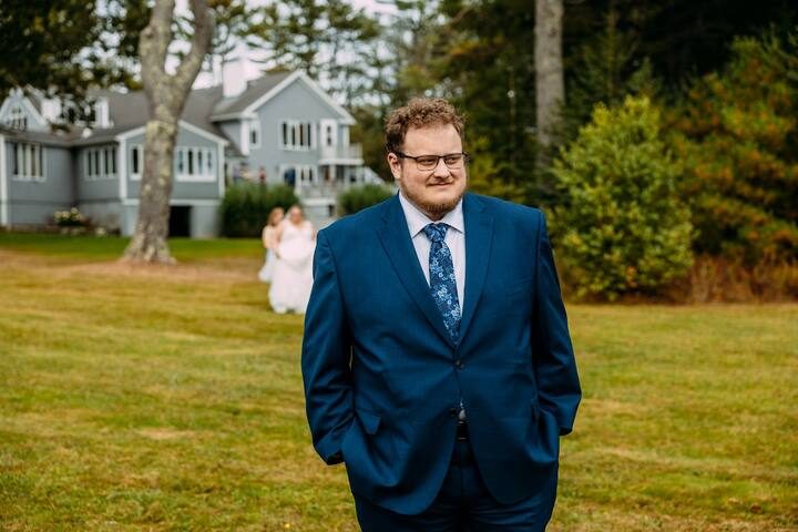 A groom stands on the lawn with the estate house behind him