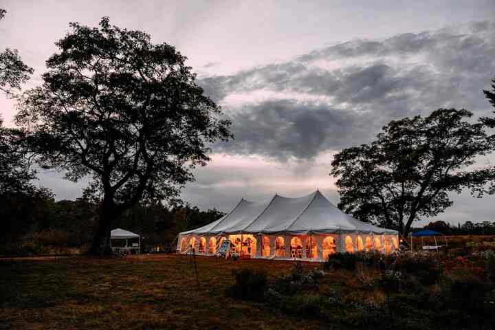 The sailcloth tent glowing from within at dusk, framed by silhouetted trees under a dramatic sky