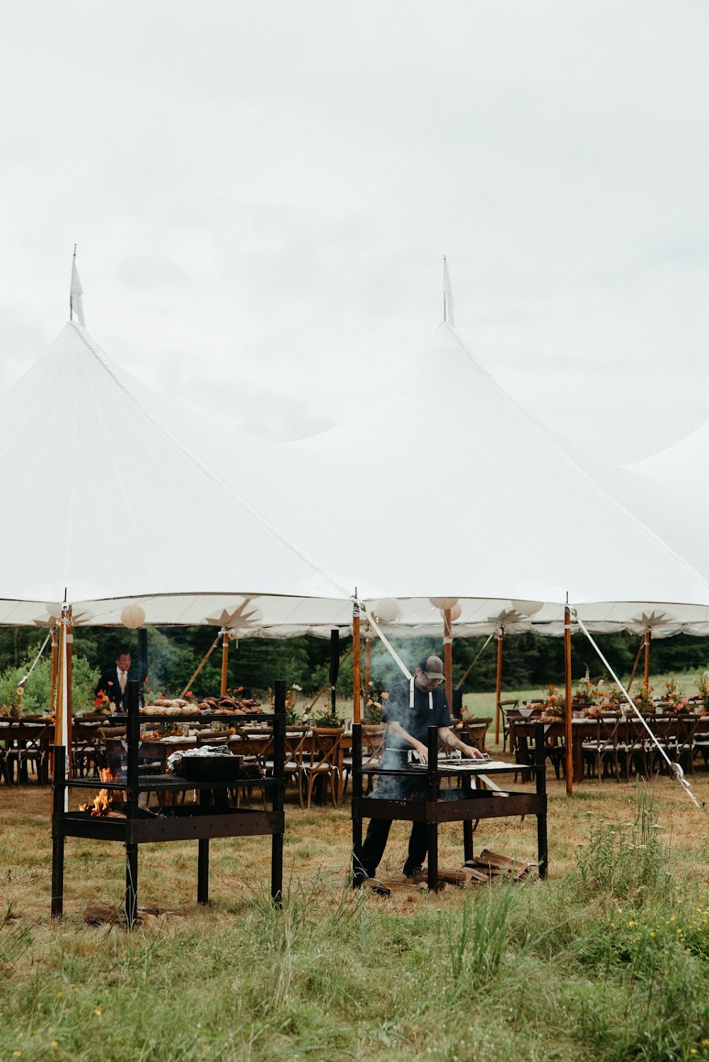 Two open-fire grill stations set up in front of the sailcloth reception tent