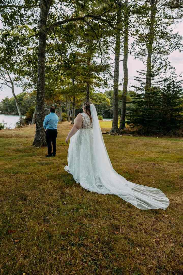 A bride in her gown approaches her groom in the trees during a fall first look