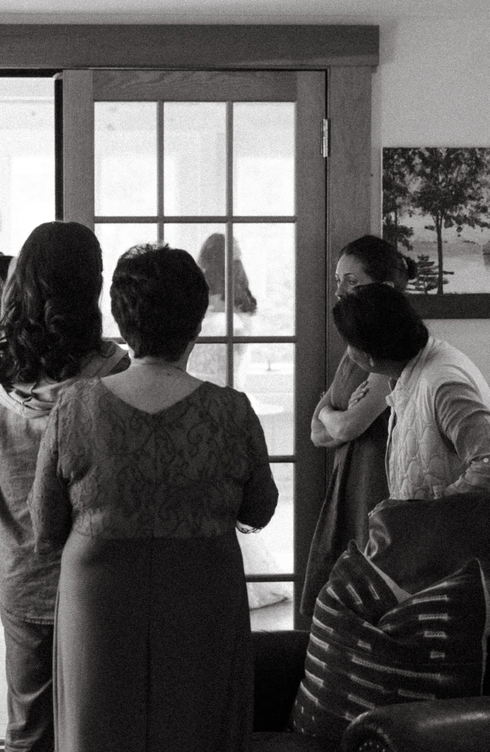 Bridesmaids look out a window watching the ceremony begin, black and white photo