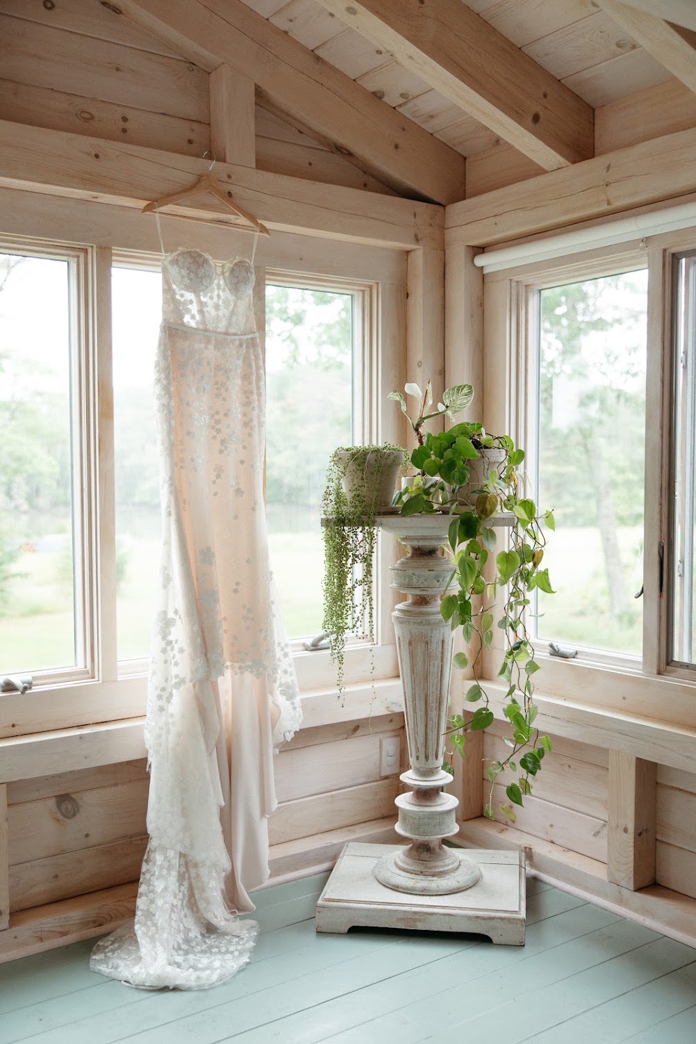 A wedding dress hangs by the barn's corner windows next to trailing houseplants