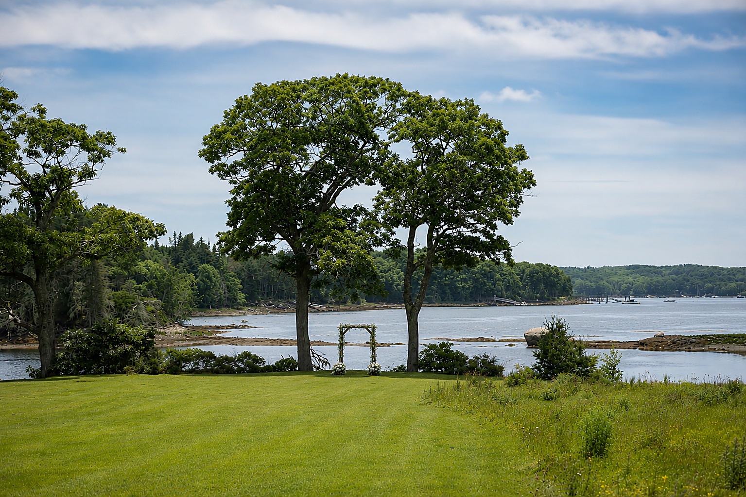 Ceremony arbor framed by two oak trees on the shore of Pemaquid Harbor