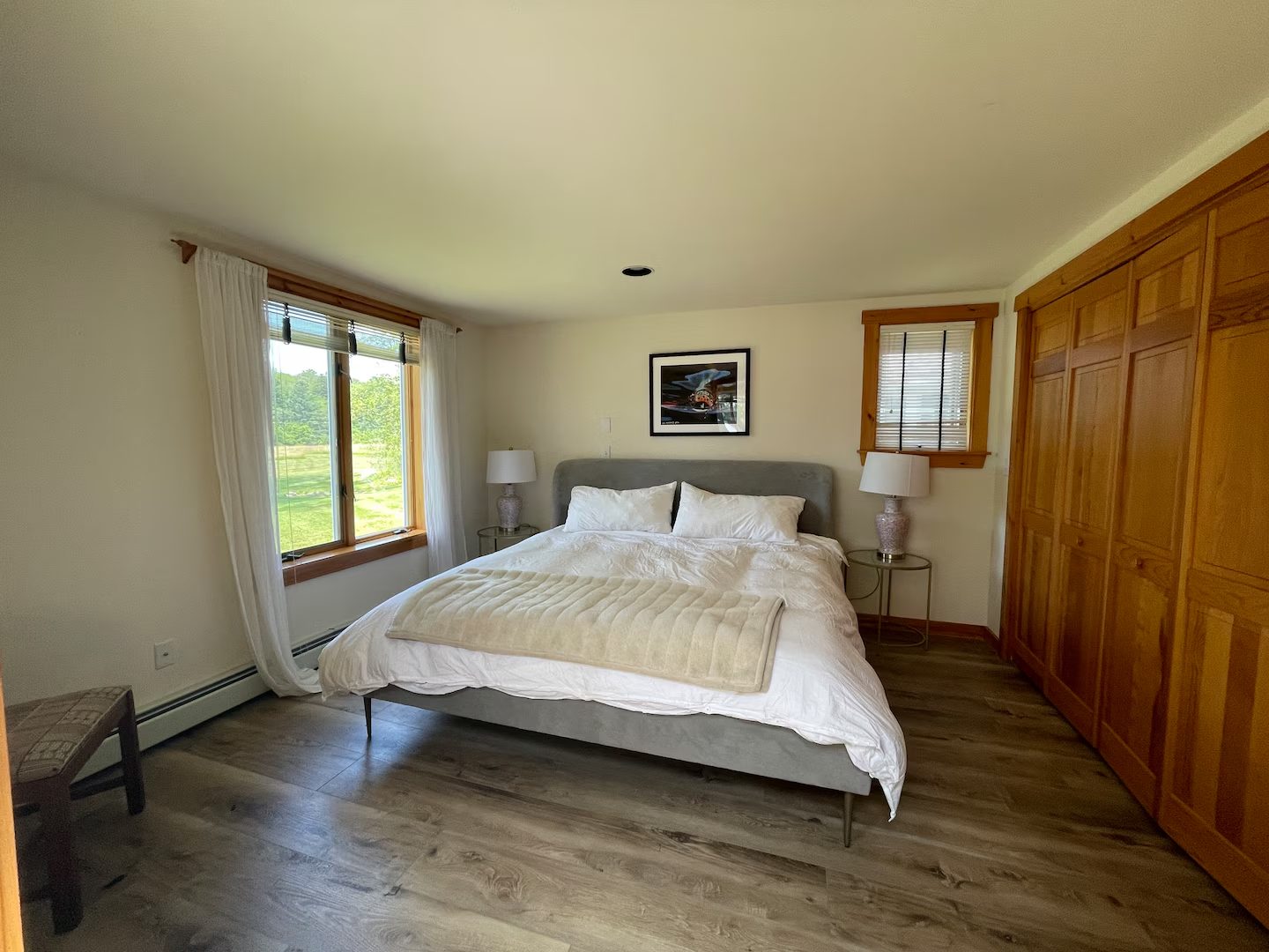A guest bedroom with a upholstered bed frame and a window looking over the lawn