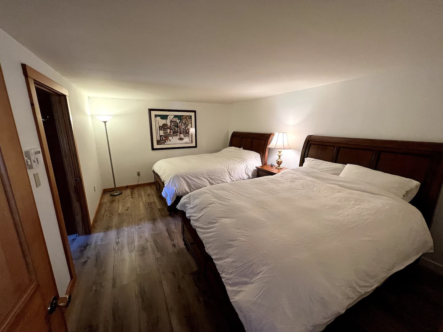 A bedroom with two queen beds, wood sleigh-style frames, and a reading lamp between them