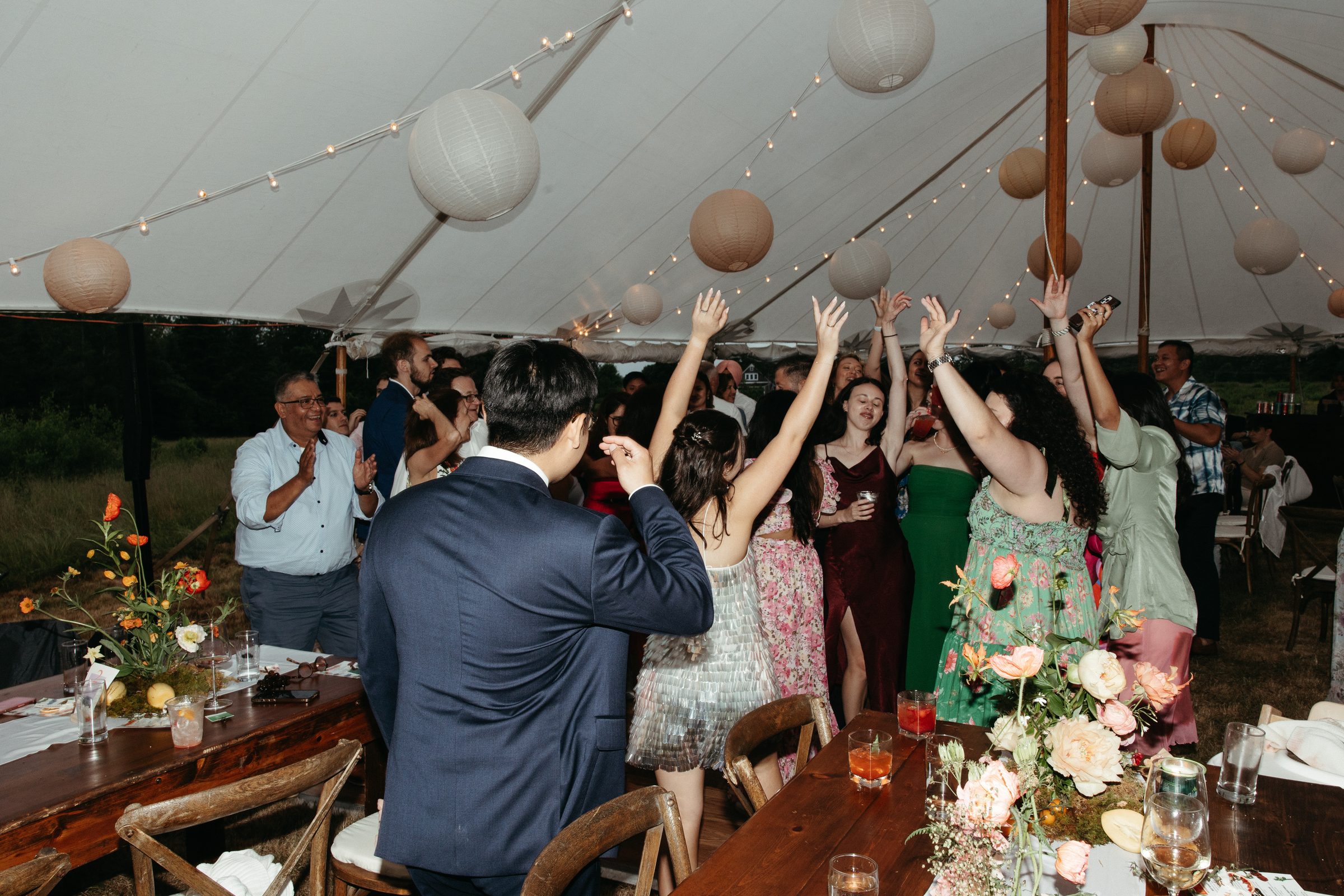 Guests dance with hands raised under paper lanterns strung inside the tent