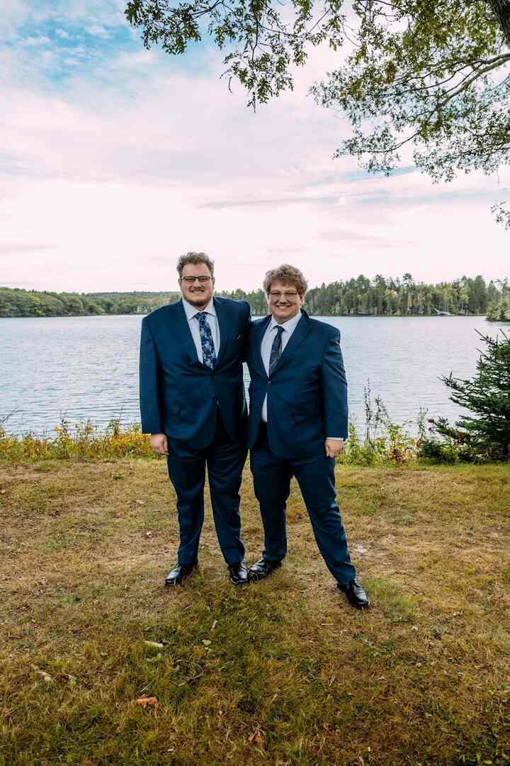 Two groomsmen in navy suits stand together by the water
