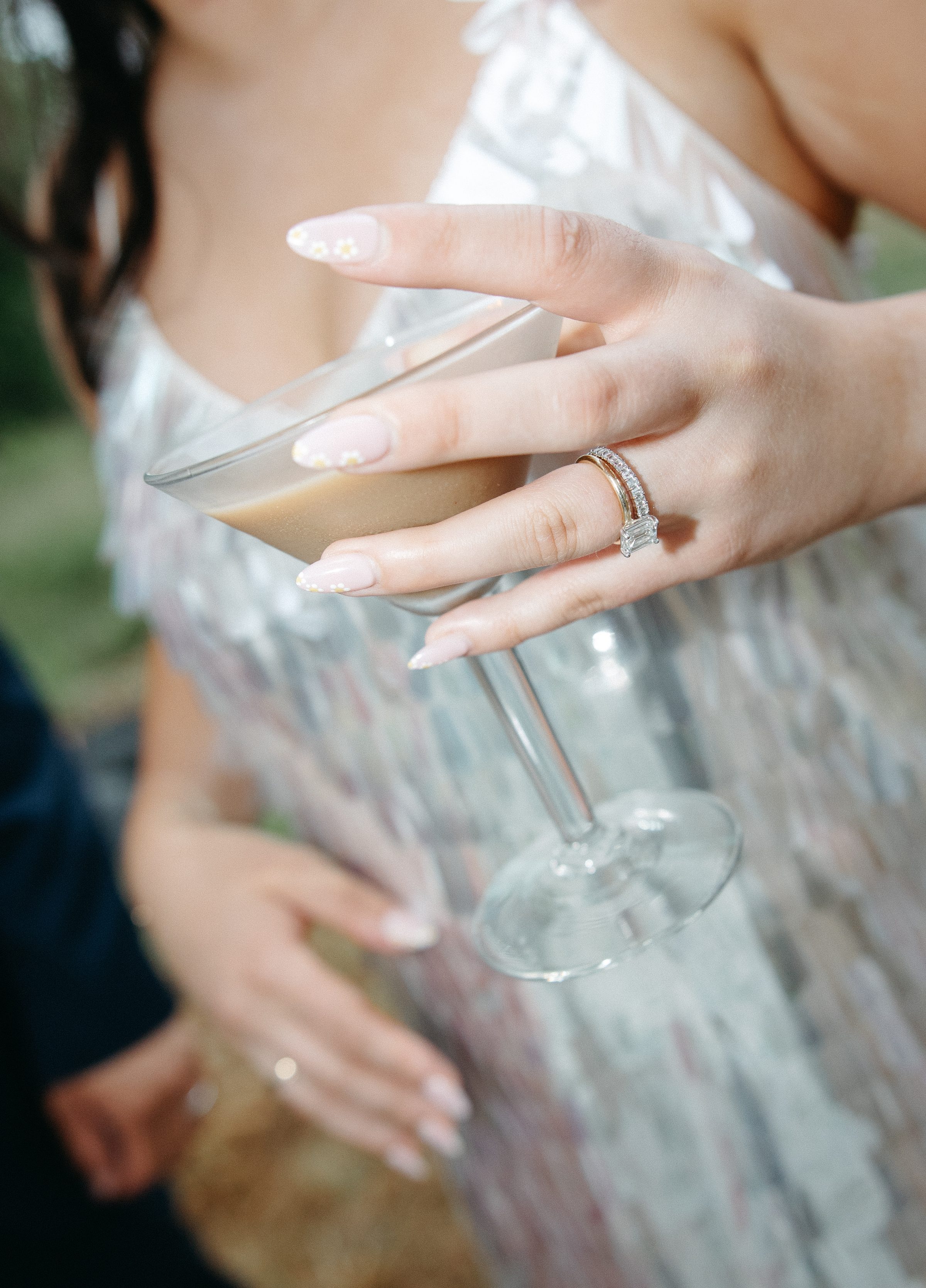 A close-up of a bride's hand holding a cocktail, wedding ring visible